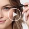 Model trägt Wimpernspülung auf und Play-Taste in der Mitte